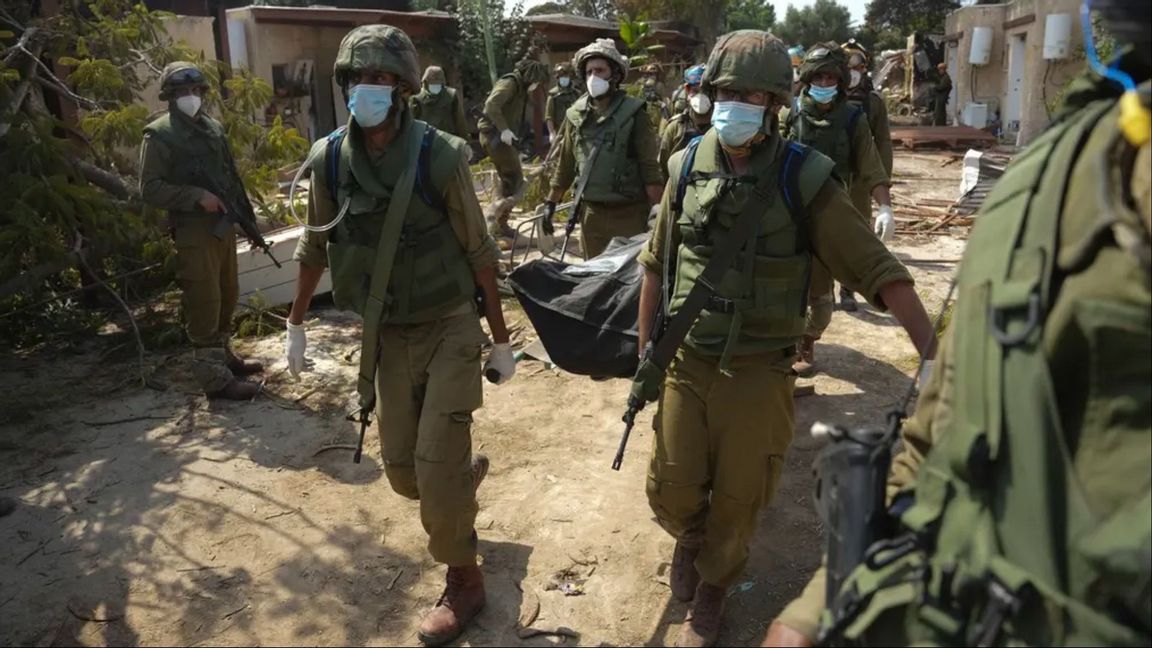 Israeliska soldater bär bort lik i Kfar Azza i södra Israel efter lördagens massaker mot byns invånare. Foto: Erik Marmor/AP/TT