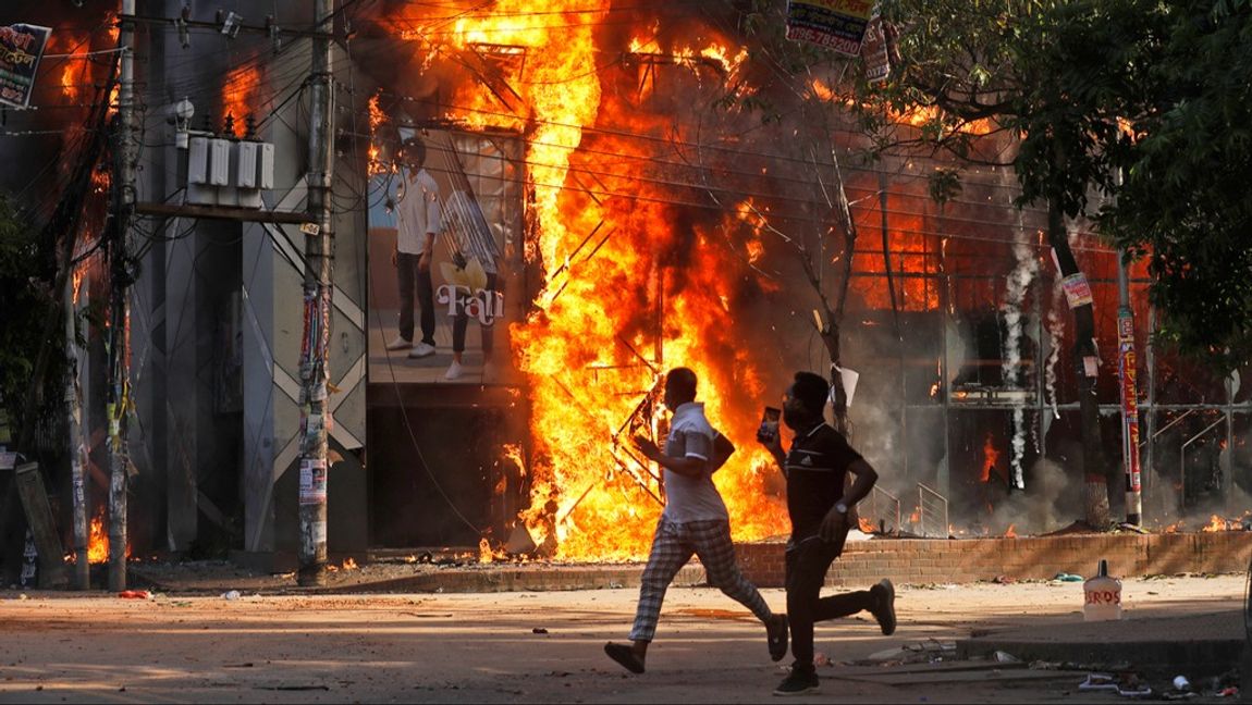 Två män springer under söndagen förbi ett köpcentrum som satts i brand under protesterna i Bangladesh. Foto: RAJIB DHAR/AP/TT