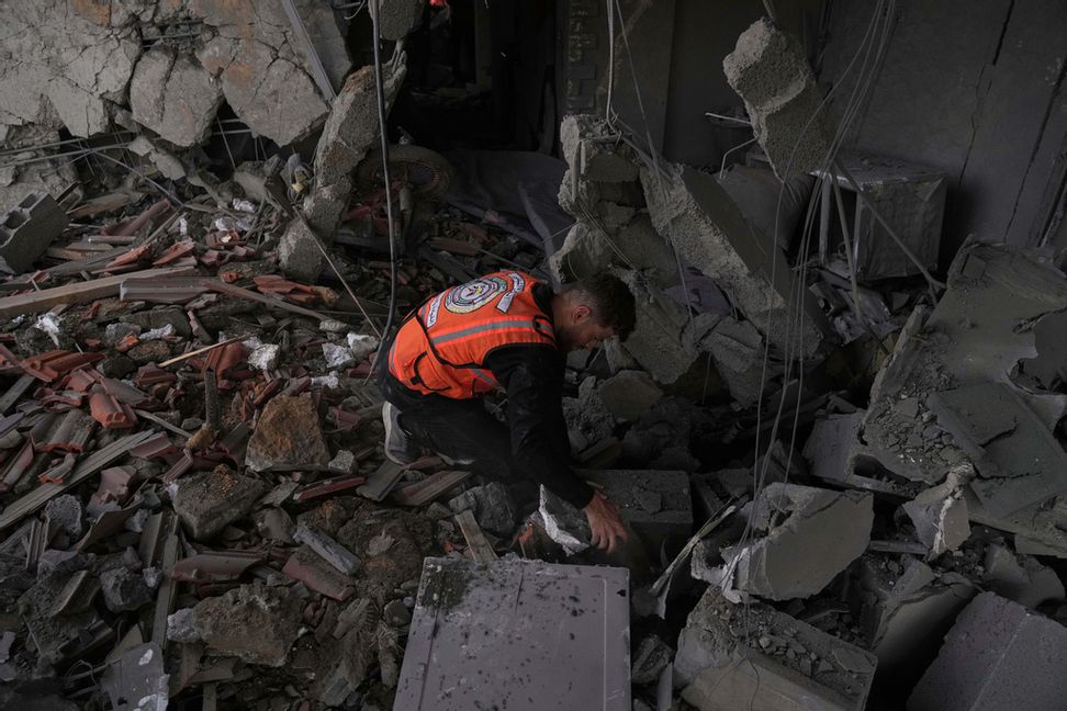 En anställd vid palestinska civilförsvaret letar igenom rasmassorna efter ett israeliskt luftangrepp mot ett bostadshus i staden Gaza under torsdagen. Foto: Jehad Alshrafi/AP/TT
