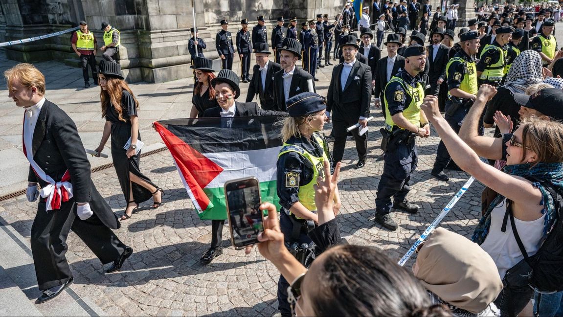 En nypromoverad doktor i fysik vecklar ut en palestinaflagga utanför Lunds domkyrka Foto: Johan Nilsson/TT