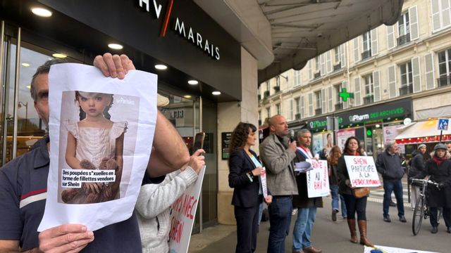 Protester utanför byggnaden där den nya Shein-butiken ska öppnas i Paris. En man håller upp en bild på en barnliknande sexdocka som har funnits till försäljning på e-butikens hemsida. Foto: Nicolas Garriga/AP/TT