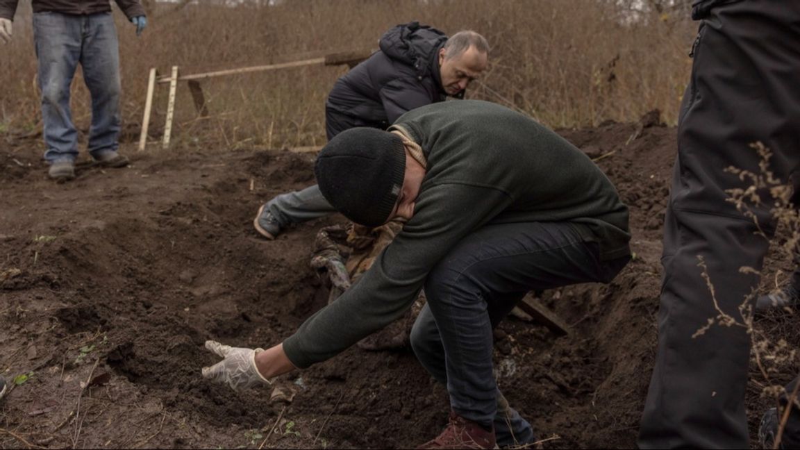 En frivillig som hjälper till att gräva ut en massgrav utanför Cherson i måndags får kväljningar av liklukten Foto: Roman Pilipey/EPA/TT