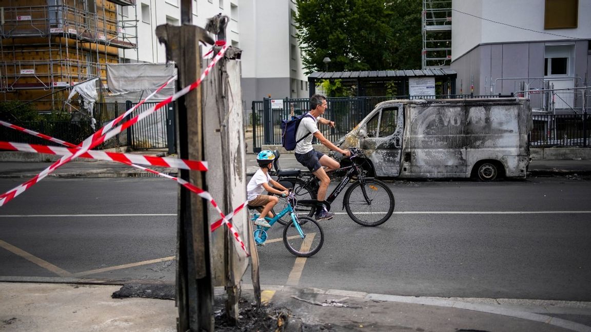 En pappa med son cyklar förbi en uppbränd bil i utkanterna av Paris. Foto: Christophe Ena