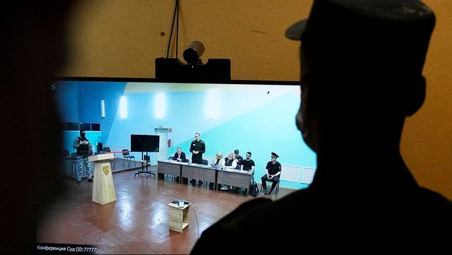 En vakt står framför en tv där Aleksej Navalnyj syns föra sin egen talan i en rättssal i fängelset där han hölls i Melechovo öster om Moskva. Arkivbild från juni i år. Foto: ALEXANDER ZEMLIANICHENKO/AP/TT