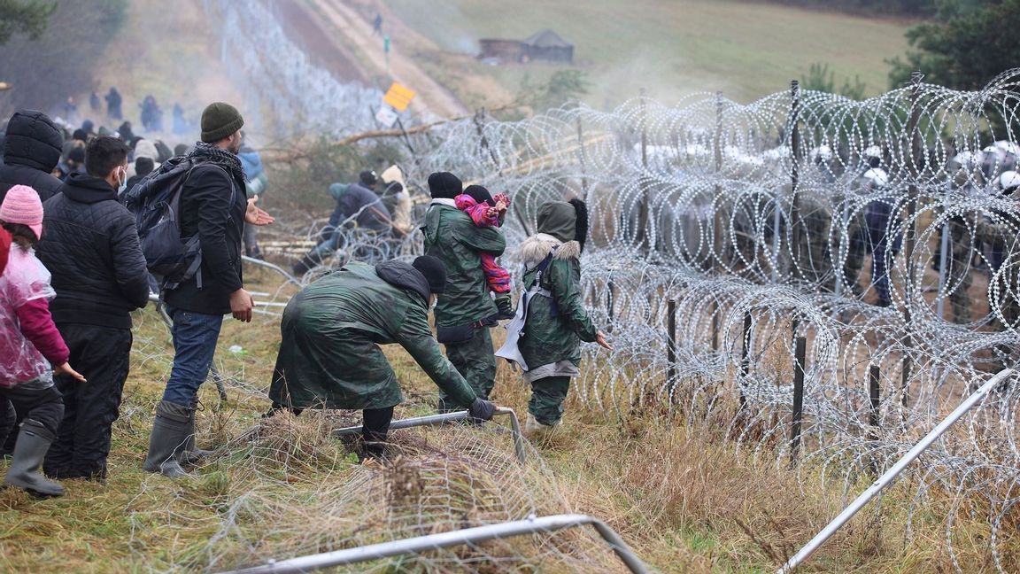 Migranter med barn vid gränsen Belarus–Polen. På andra sidan syns de polska soldaternas vita hjälmar. Foto: Leonid Sjtjeglov/AP/TT.