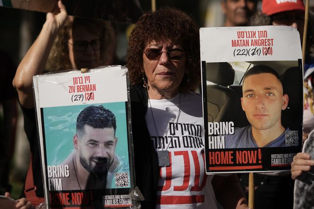 En kvinna bär på porträtt av Ziv Berman och Matan Angrest under en demonstration den 7 oktober. De båda männen tillhör de 20 ur gisslan som tros vara vid liv. Foto: Leo Correa/AP/TT