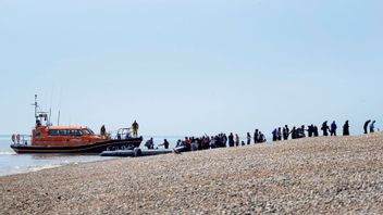Personer som tros vara migranter stiger i land på Dungeness-udden i sydöstra England under uppsikt av sjöräddningsorganisationen Royal National Lifeboat Institution. Cirka 50 personer korsade Engelska kanalen i samma uppblåsbara båt under måndagen. Foto: Gareth Fuller/AP/TT.