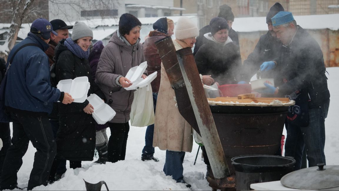 Volontären Marat Darmenov till höger delar ut gratis varm mat i Kiev under ett långvarigt strömavbrott till följd av nya ryska attacker mot Ukrainas energisystem den 7 februari 2026. Inte nog med att många ukrainare plågas av strömavbrott och avsaknad av fjärrvärme, nu kommer deras köpkraft att urholkas också. Foto: AP Photo/Sergei Grits