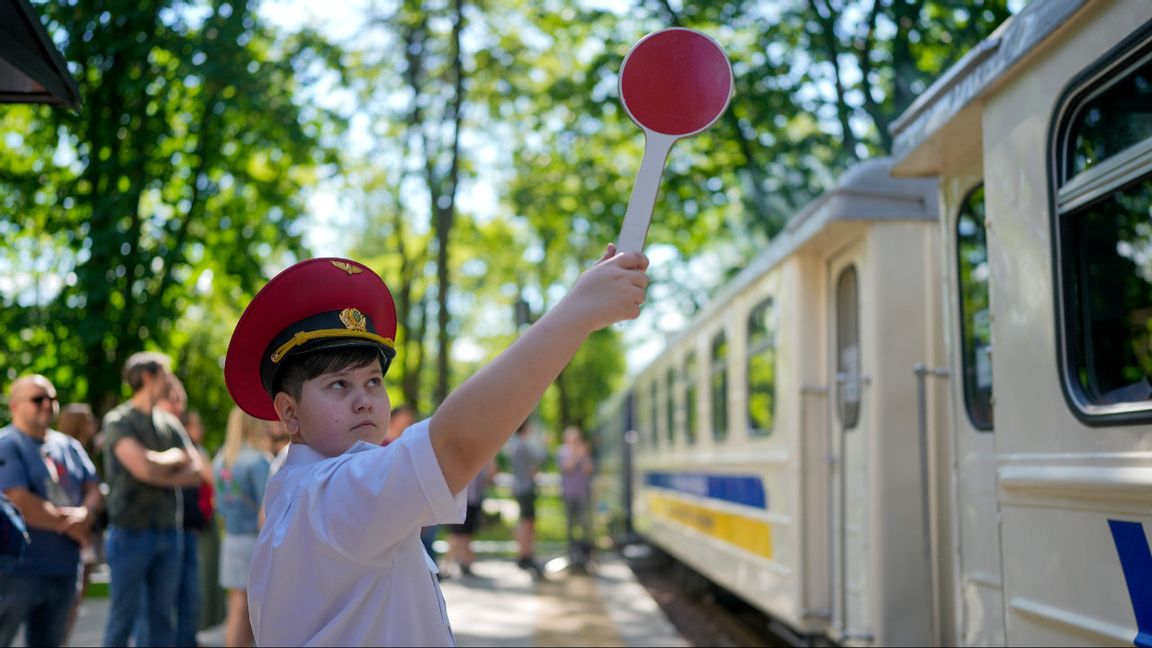 En pojke signalerar på perrongen för barnjärnvägen i Syretskyjparken i Kiev den 4 juni 2022 efter att järnvägens verksamhet legat nere under den första krigsvåren. Just den här järnvägen fyller bara funktionen som turist- och utbildningsinstitution, därför har den till skillnad från andra järnvägar i Ukraina inte attackerats. Foto: AP Photo/Natacha Pisarenko
