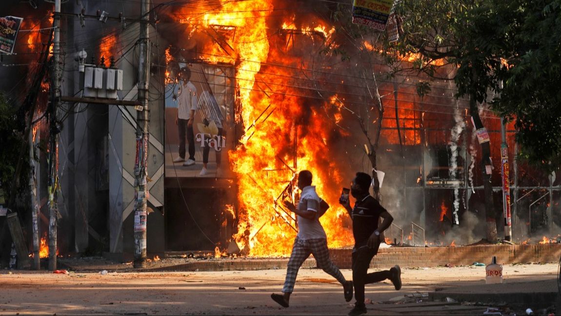 Två män springer på söndagen förbi ett köpcentrum som satts i brand under protesterna i Bangladesh. Foto: Rajib Dhar/AP/TT