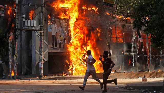 Två män springer på söndagen förbi ett köpcentrum som satts i brand under protesterna i Bangladesh. Foto: Rajib Dhar/AP/TT