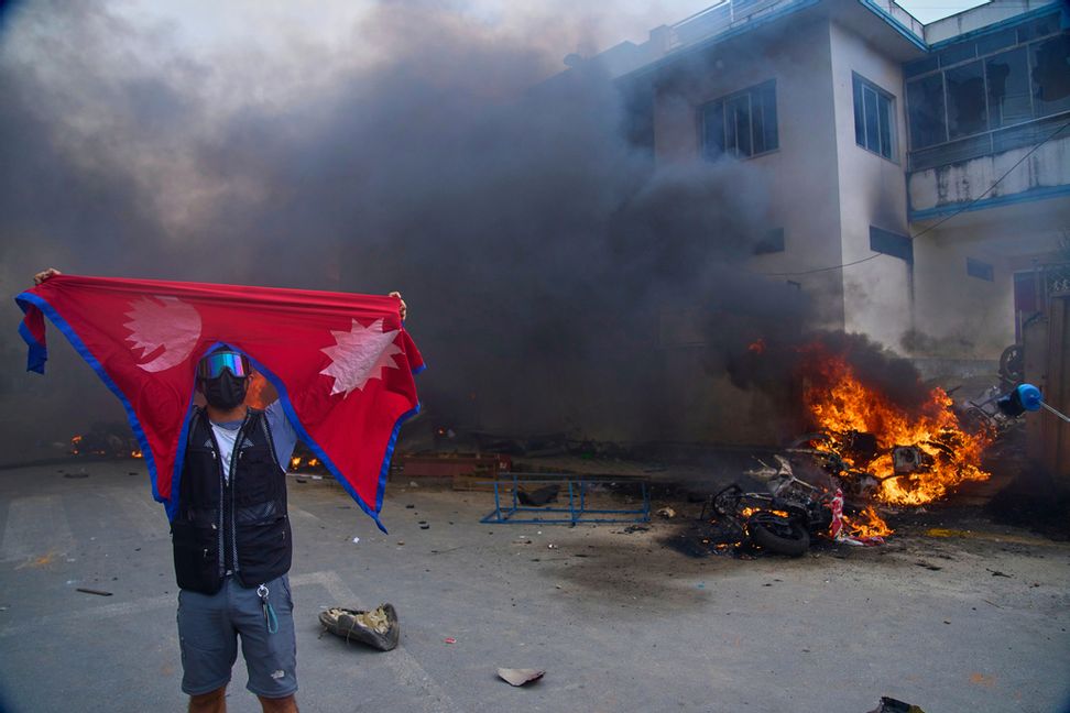 En demonstrant med Nepals flagga framför en brinnande polisstation i Katmandu. Foto: Niranjan Shrestha/AP/TT