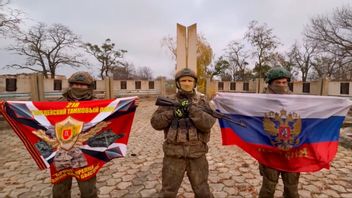 Ryska soldater firar att de gått in i byn Uspenivka i Zaporizjzjiaregionen genom att hålla upp sin förbandsflagga från det 218:e gardesstridsvagnregementet och en rysk flagga framför ett andravärldskrigsmonument den 7 november 2025. Foto: Rysslands försvarsministeriums presstjänst via AP